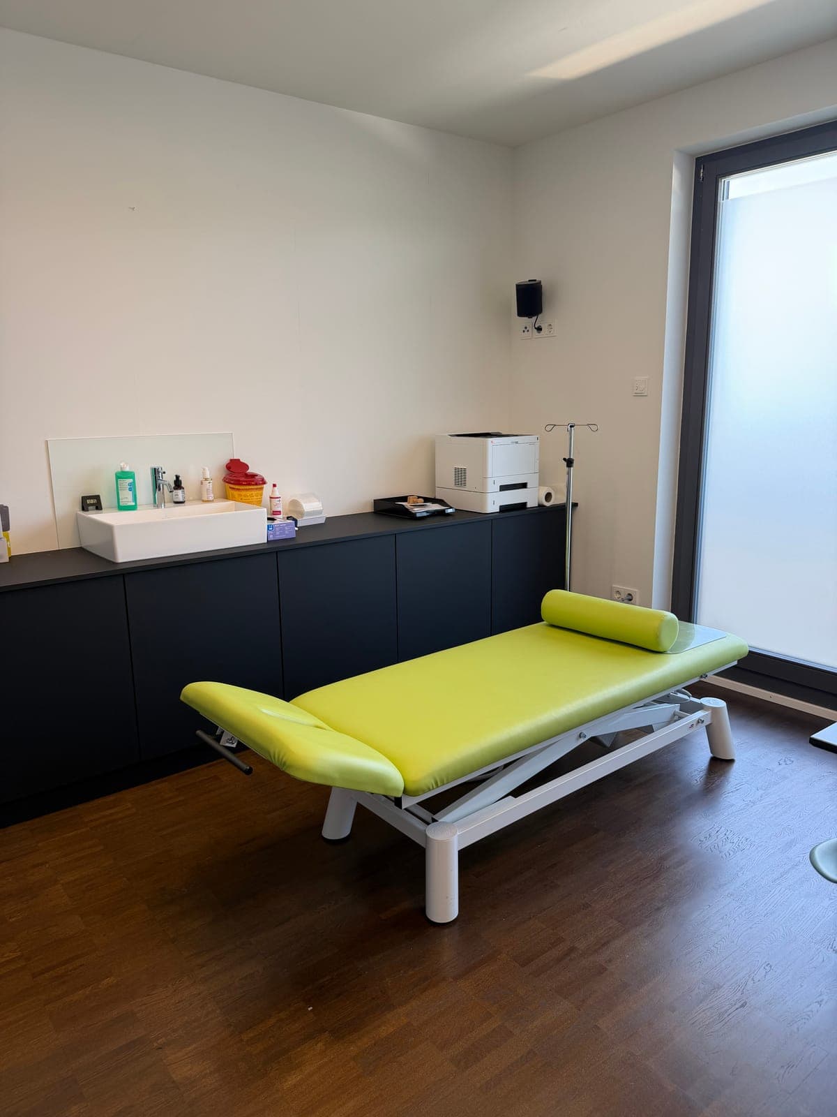 Hellgrüne Behandlungsliege vor dunkler Schrankzeile mit Waschbecken